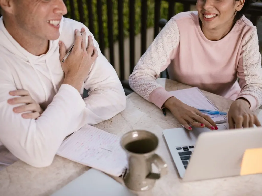 Deux personnes souriantes devant un ordinateur portable et des notes manuscrites