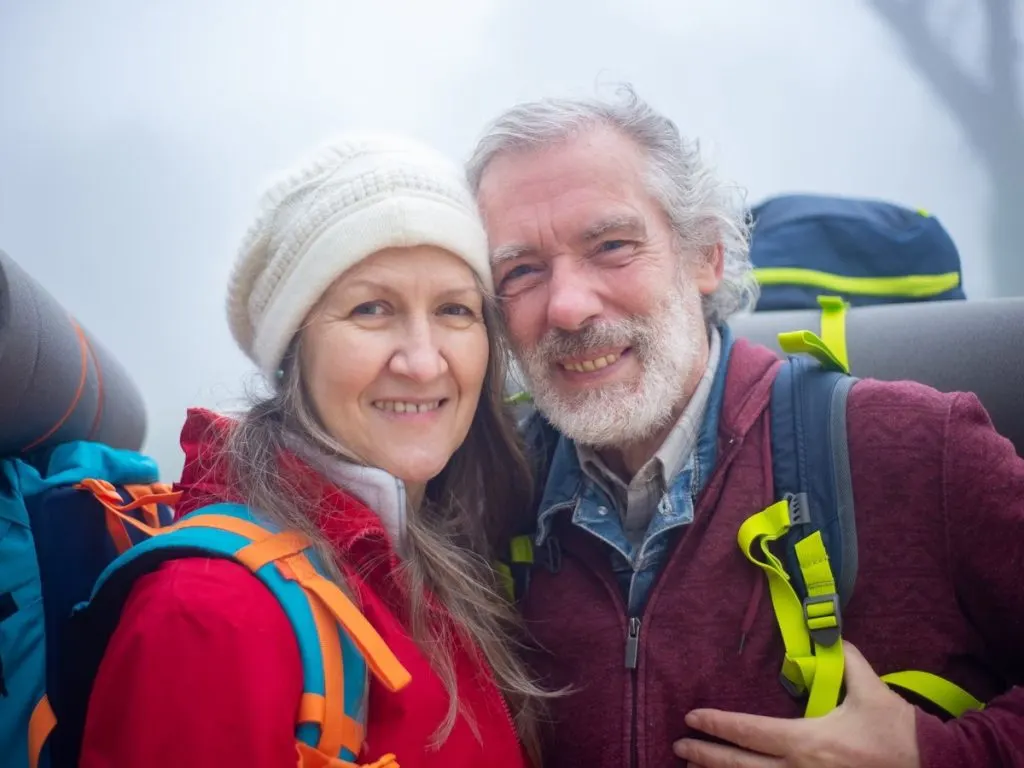 Couple de sexagénaires souriants, sac à dos, en randonnée