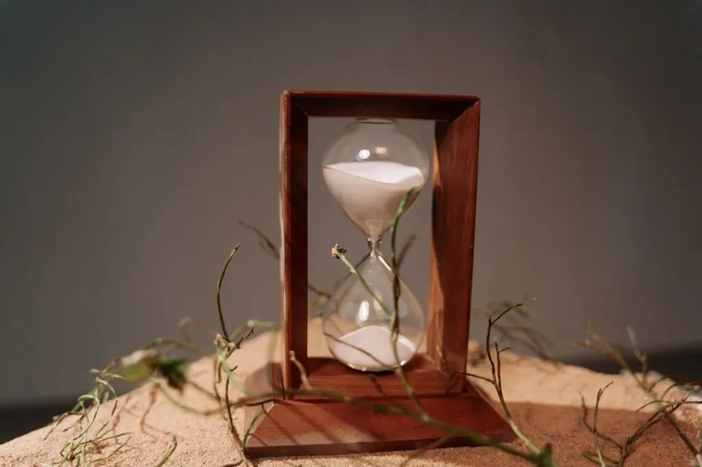 Gros plan d'un sablier en bois avec du sable qui s'écoule, symbole du temps qui passe.