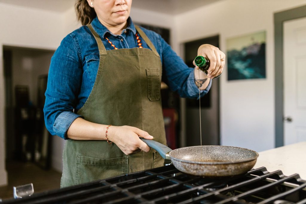 Un chef en tablier verse de l'huile d'olive dans une poêle sur une cuisinière