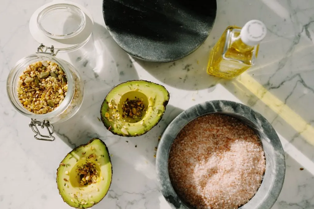 Avocat coupé en deux, graines et sel rose sur marbre blanc, vue du dessus, cadrage net