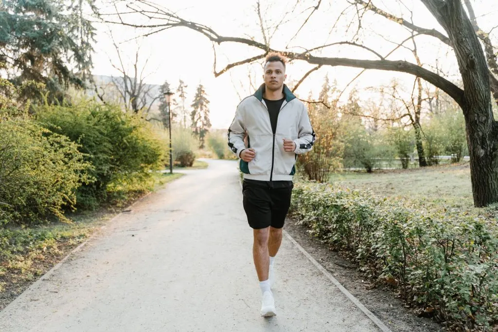 Homme adulte joggant sur un chemin de parc, lumière naturelle du matin, effort maîtrisé
