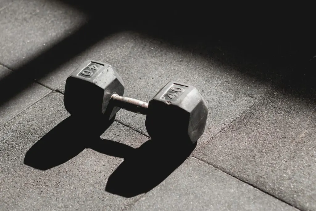 Un haltère de 40 livres posé seul sur le sol d'une salle de sport, jeu d'ombre et lumière