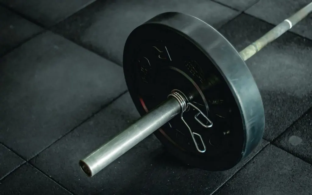 Barre olympique chargée d’un disque, posée au sol d’une salle d’entraînement