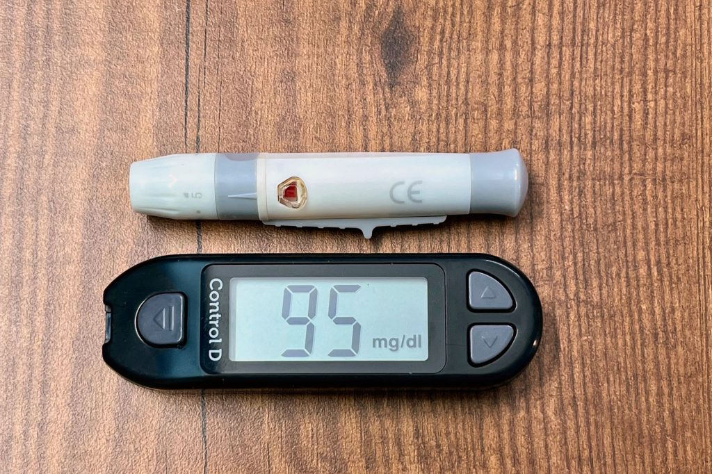 Gros plan d'un glucomètre affichant 95 mg/dl avec un stylo autopiqueur, sur fond neutre