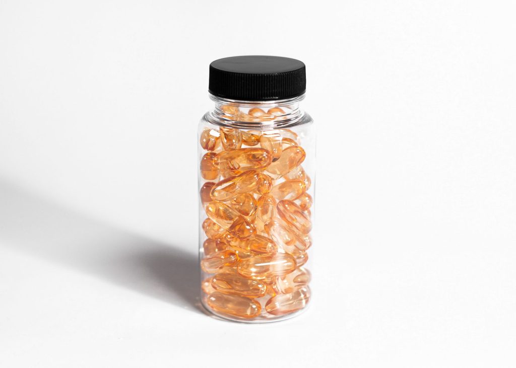 Bouteille transparente remplie de capsules ambrées sur fond blanc, gros plan sobre