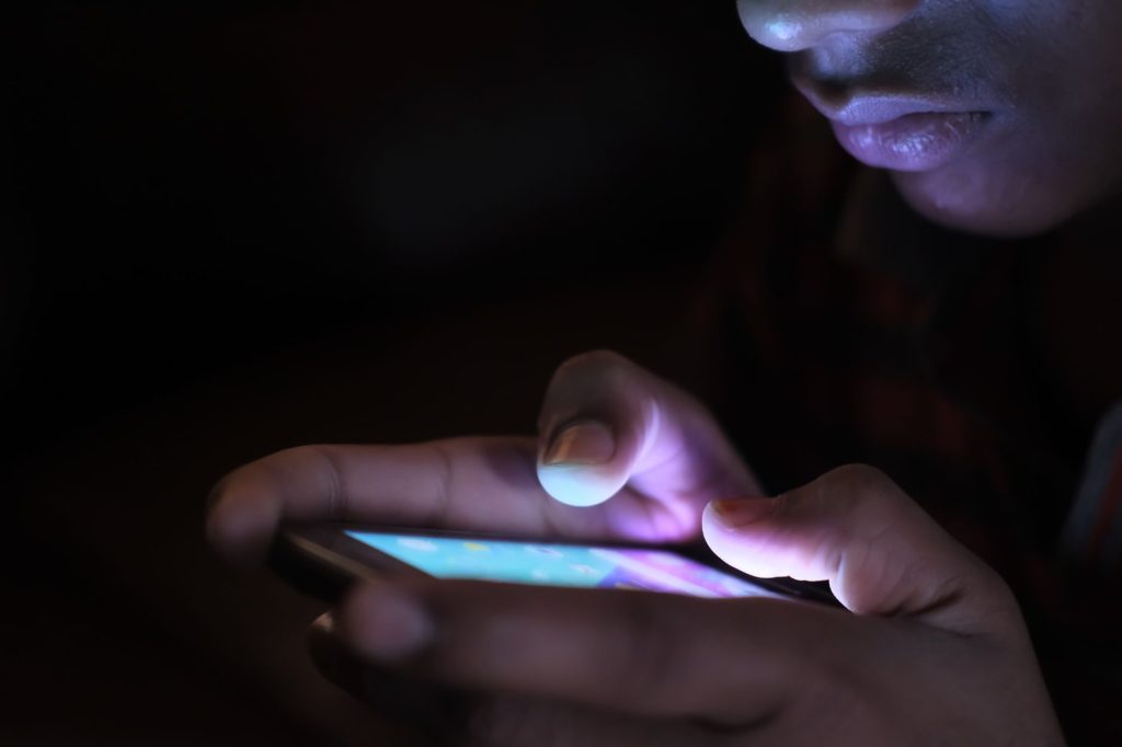 Gros plan d'une main tenant un smartphone allumé dans l'obscurité, sans visage visible