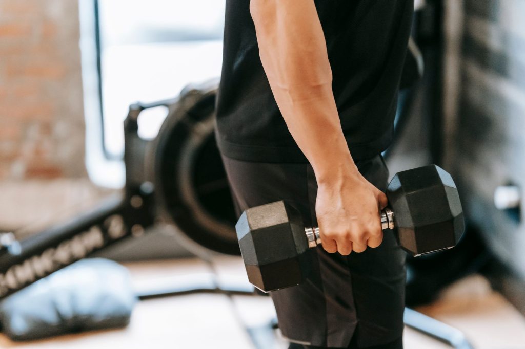 Vue de profil d'un homme musclé en tenue noire soulevant une charge lourde dans une salle de sport épurée
