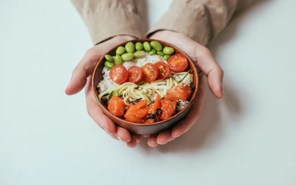 Bol de riz, saumon, tomates et edamame tenu à deux mains