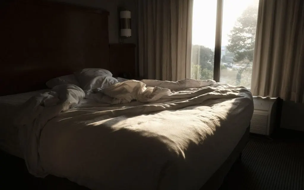 Lit défait au petit matin, lumière du jour filtrant par la fenêtre