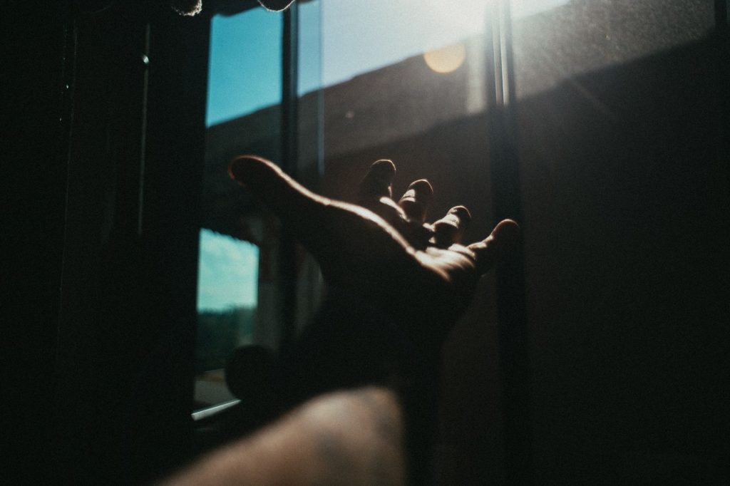 Silhouette dramatique d'une main tendue vers la lumière du soleil filtrant à travers des stores, ombre marquée