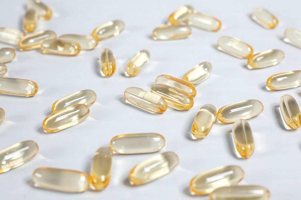 Gros plan de capsules jaunes translucides de vitamine D sur fond blanc, style pharmaceutique épuré