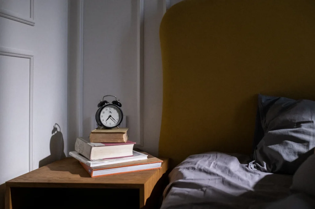 Une table de chevet cosigne avec des livres et un réveil près d'un lit, ambiance sobre
