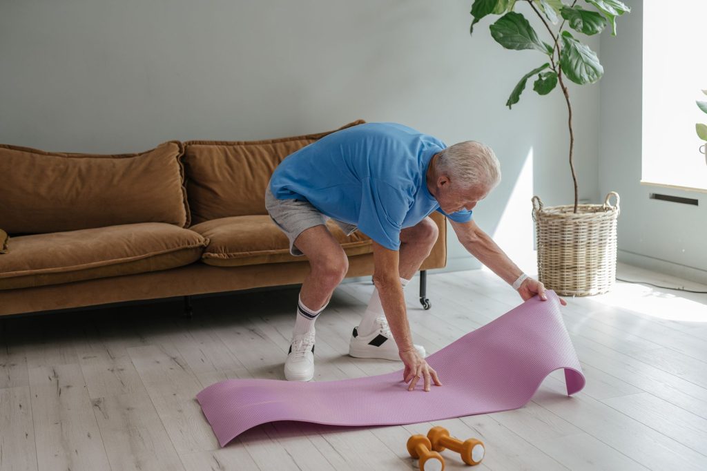 Un homme senior installe son tapis de yoga en intérieur, geste simple et actif