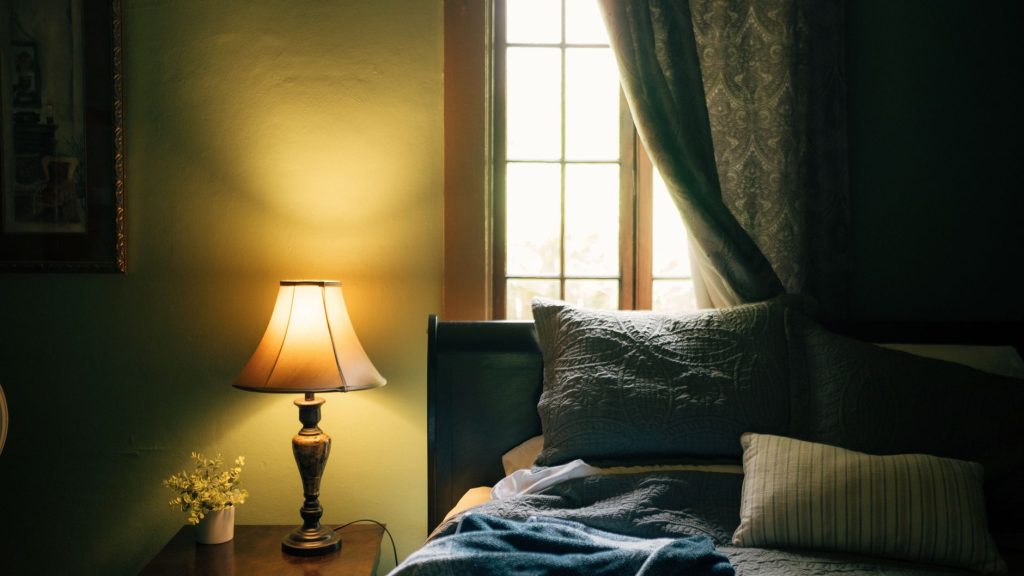 Chambre tamisée sobre avec lampe allumée, coussins et rideaux, ambiance calme du soir