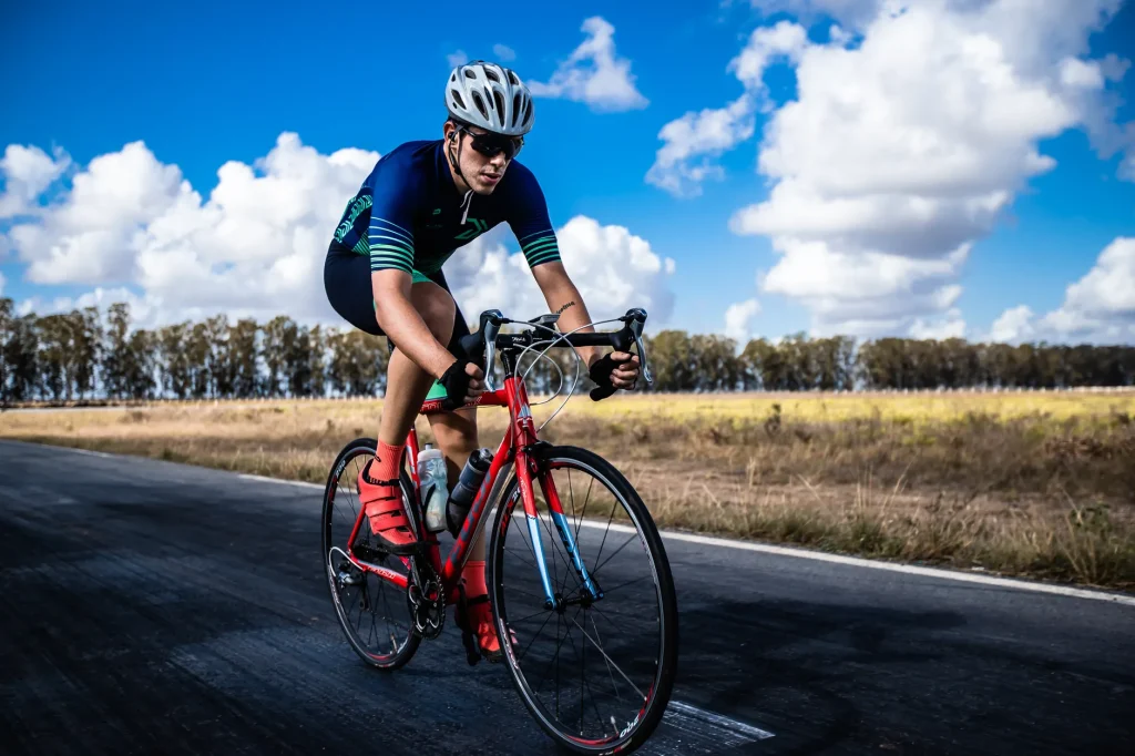 Cycliste concentré en casque roulant sur une route de campagne sous un ciel lumineux